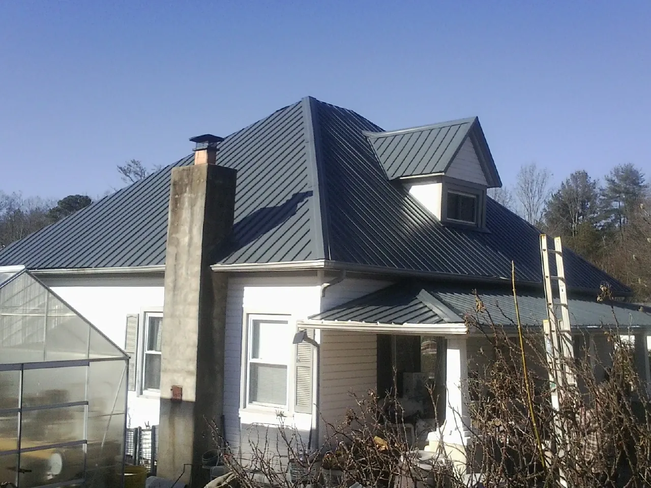 Dark blue standing seam metal roof on a white farmhouse with dormer — Slate & Tile Roof Repair by Roofing Brothers in Galveston