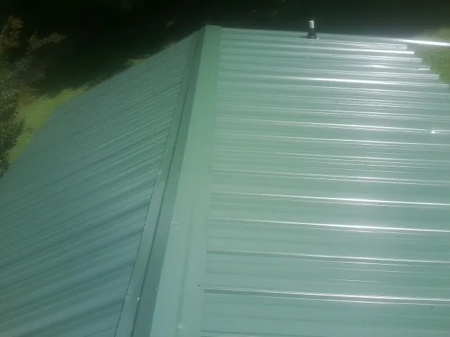 New green metal panels meeting at the ridge of a roof — Flat Roof Repair work by our crew in Galveston