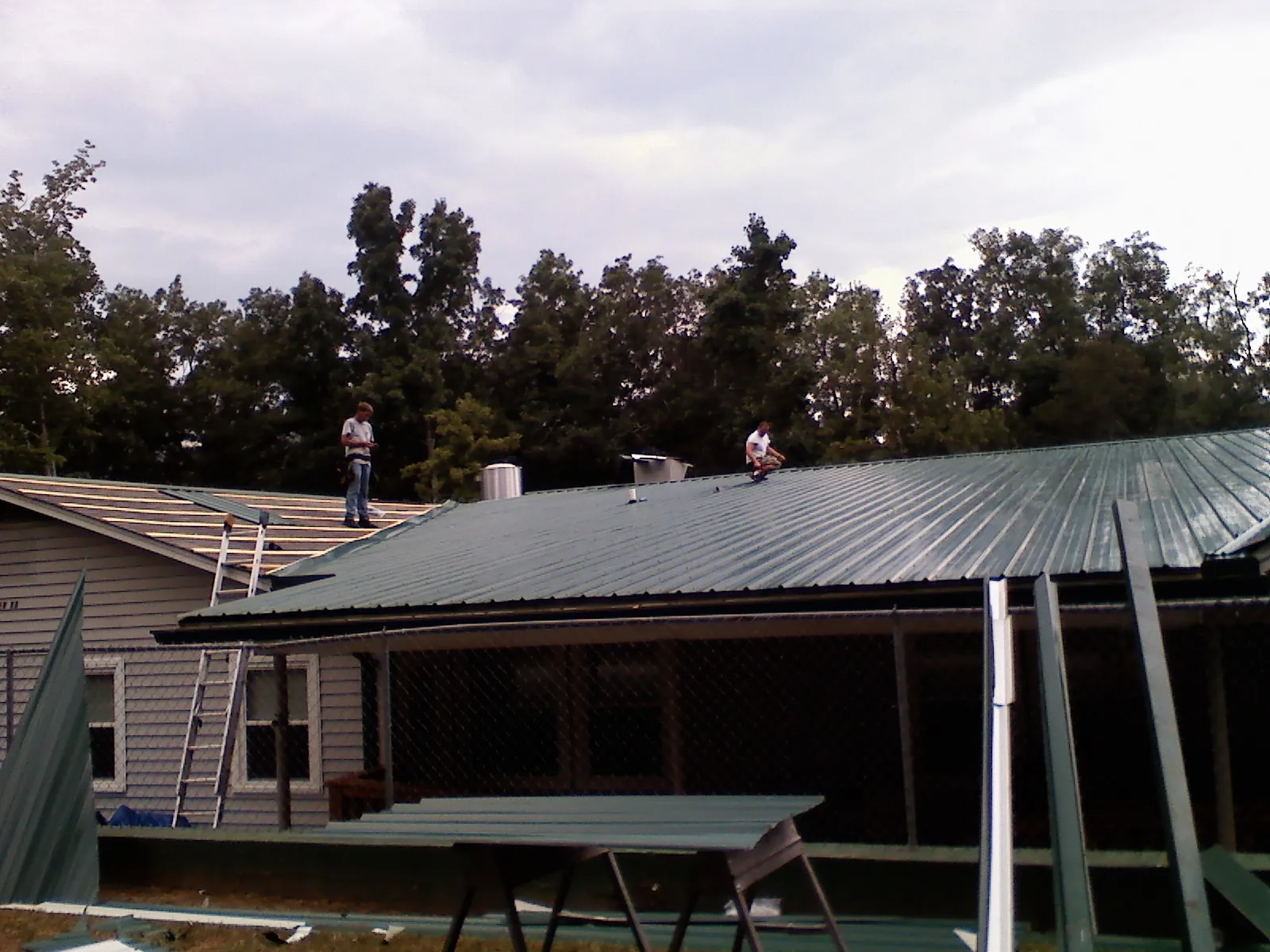 Two roofers installing green metal panels above a covered porch in Galveston