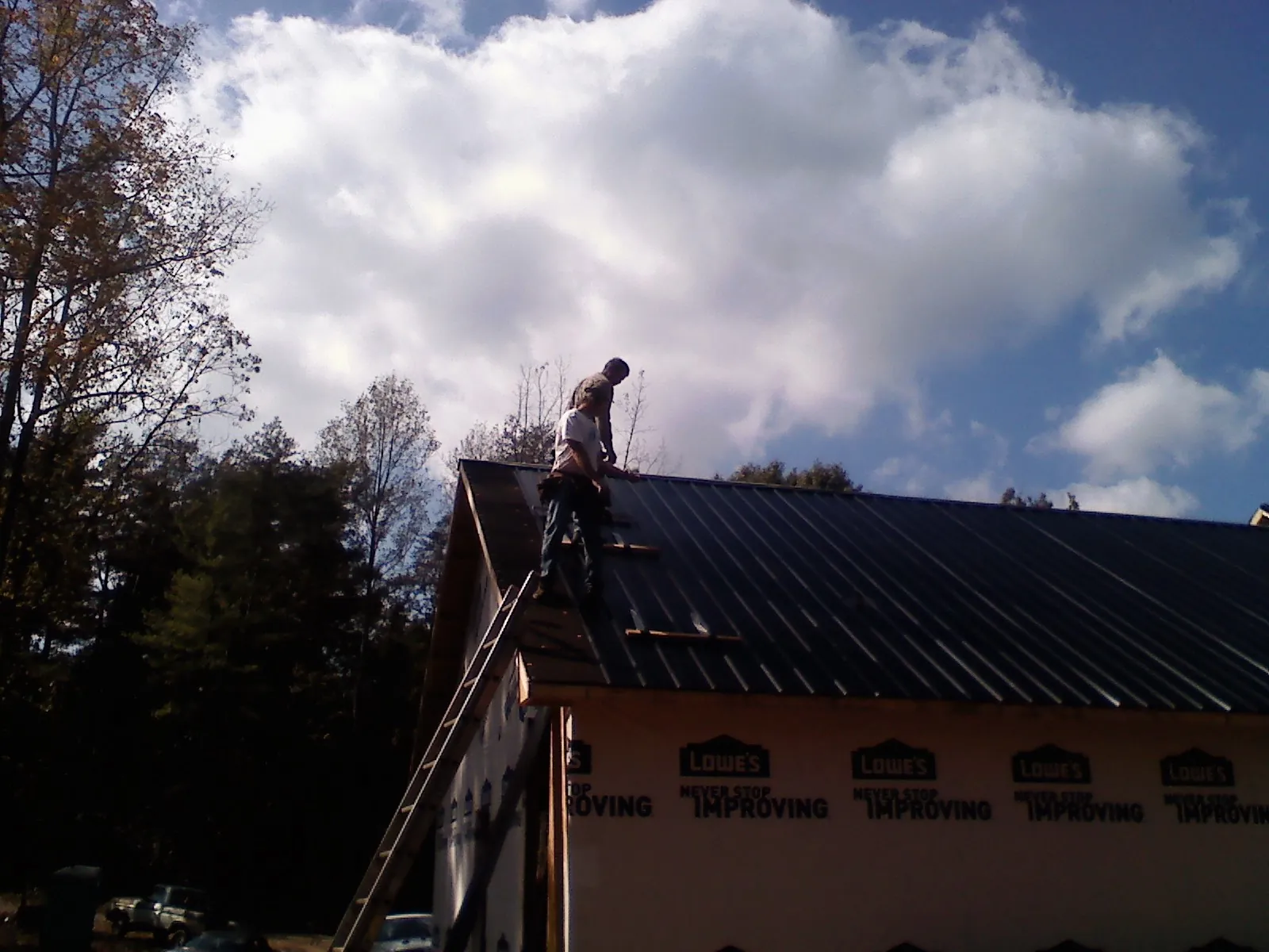 Roofer fastening dark metal panels high against a cloudy sky, from a Roof Inspection job in Galveston