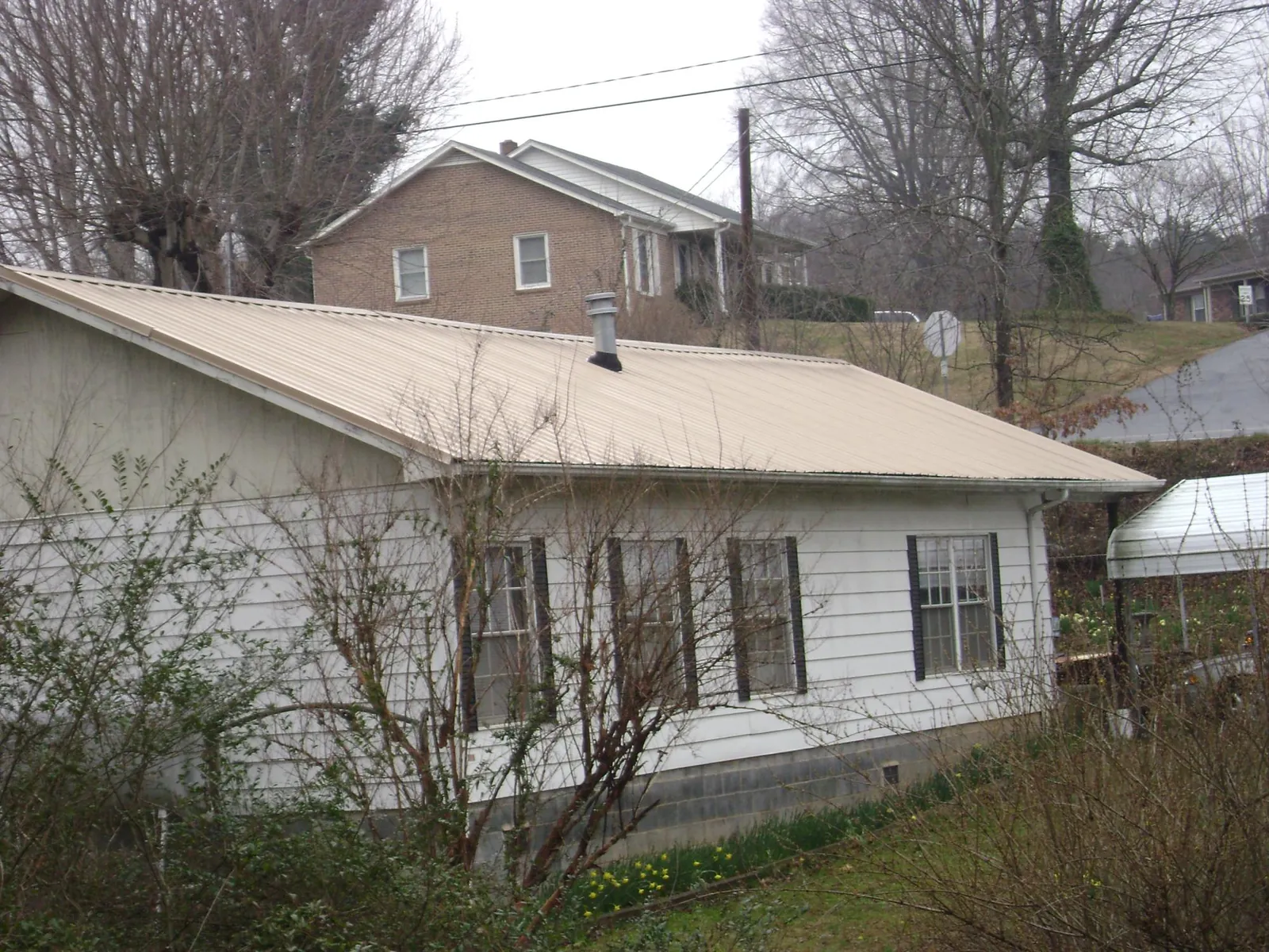 Tan metal roof on a white sided house set into a hillside — Commercial Roofing by Roofing Brothers in Galveston